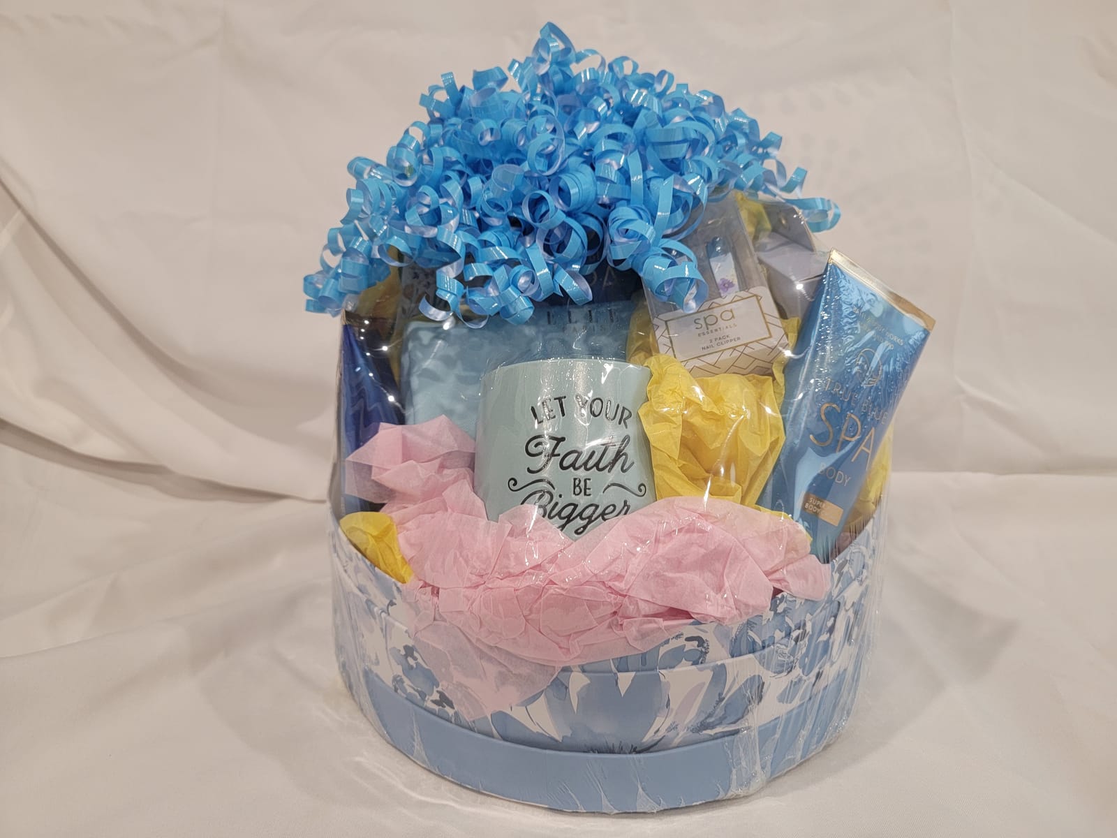 A Mother's Day gift basket with a blue bow, a Faith mug and pink tissue paper